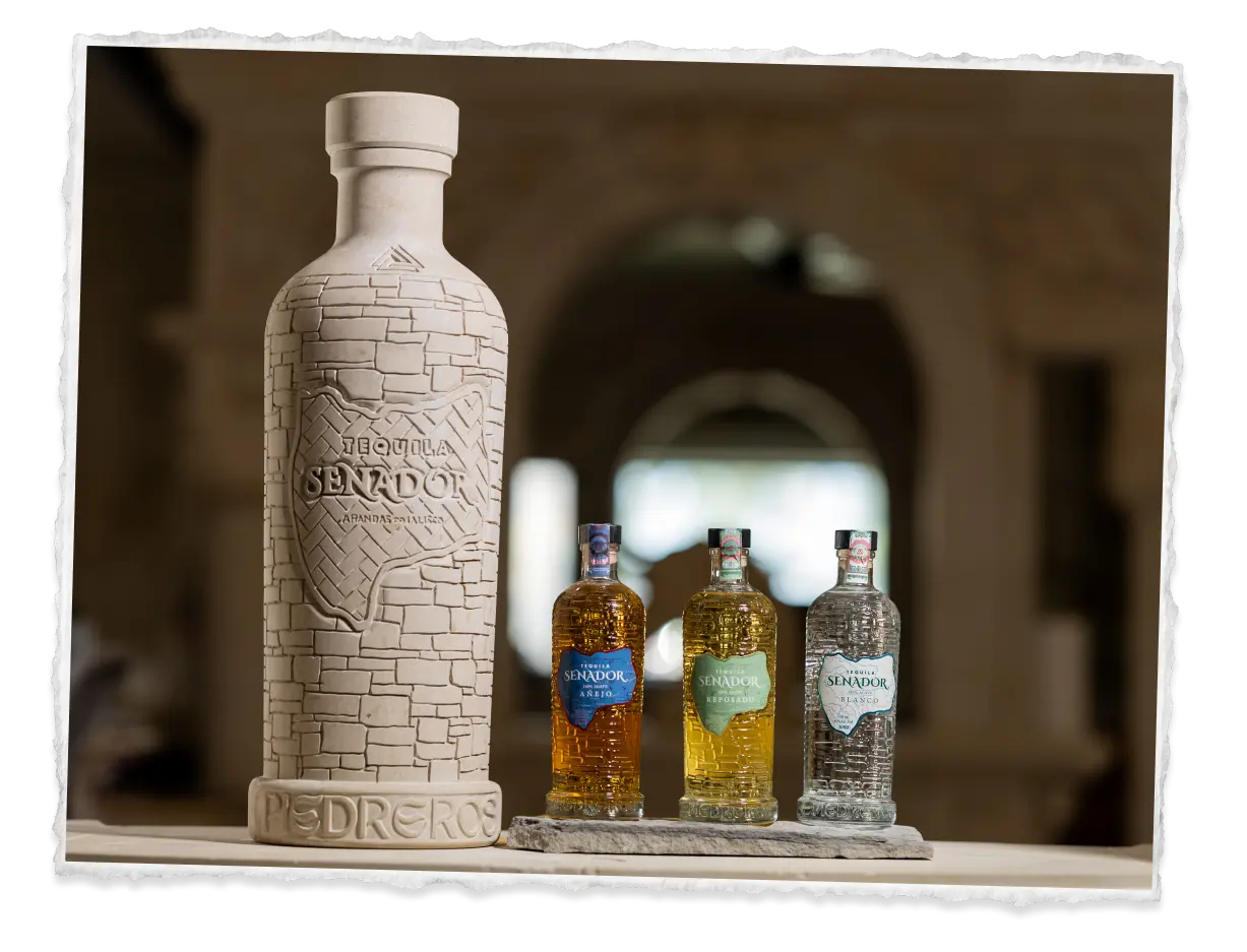 The carved stone Senador bottle on its PIEDREROS base in a vaulted hall, with Blanco, Reposado and Añejo beside it